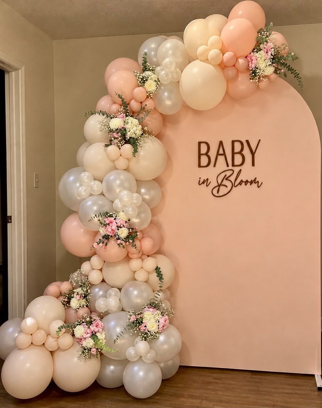 Peach arch backdrop with a Baby in Bloom sign and a peach and cream balloon garland