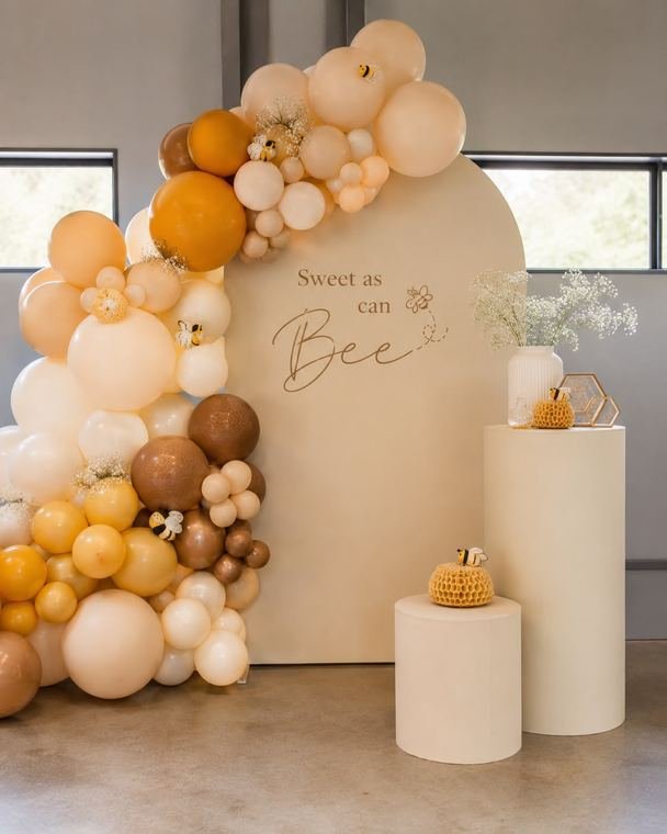 Sweet as can Bee arch backdrop with honey, mustard and cream balloons, bee accents and cream plinths