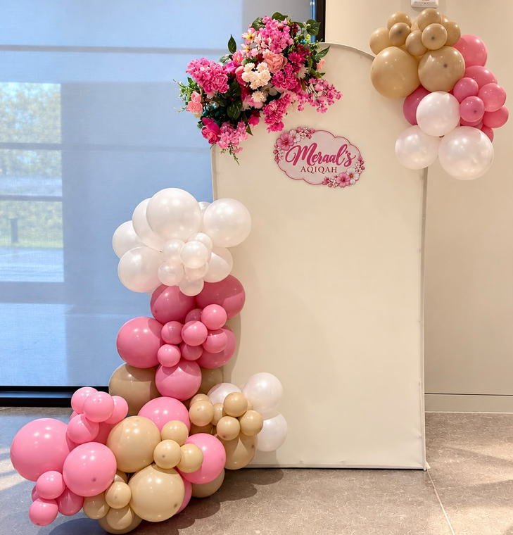 Aqiqah backdrop with a custom name sign, a pink, white and tan balloon garland and bright pink florals