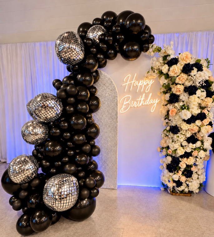 Black and chrome disco ball balloon garland beside a Happy Birthday neon sign