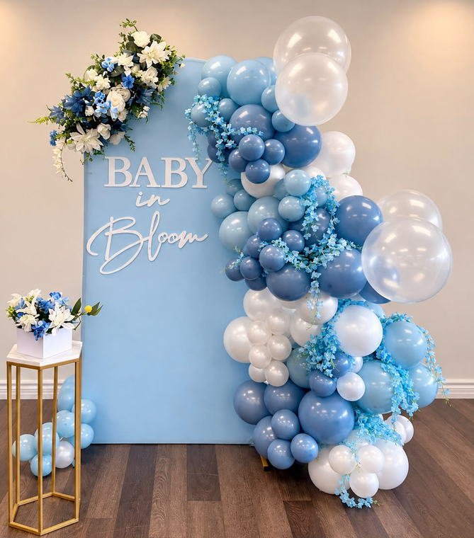 Blue Baby in Bloom baby shower backdrop with a dusty blue and white balloon garland, silk florals and a gold plinth